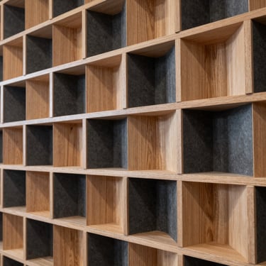 Close-up architectural detail of a geometric wood acoustic diffuser panel, sharp high-contrast lighting highlighting the natural timber grain and deep slate shadows