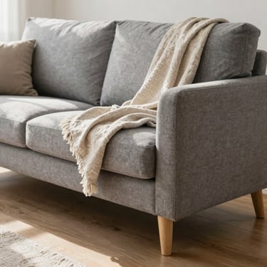 Comfortable modern grey fabric sofa with wooden legs, styled with a soft linen throw blanket, sunny living room