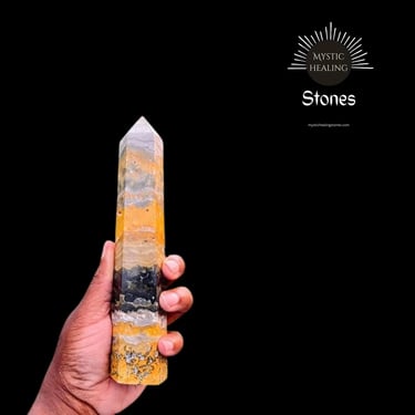 Hand holding a polished bumblebee jasper crystal point for healing and meditation.