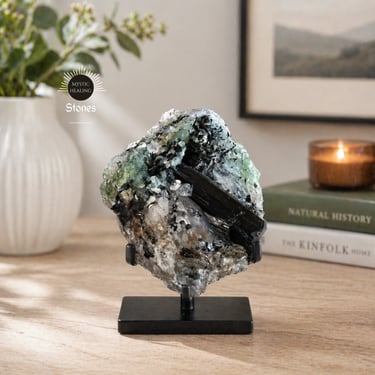 A raw black tourmaline in quartz crystal cluster displayed on a black metal stand for home decor.