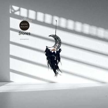 Obsidian crescent moon dreamcatcher with feathers hanging against a wall with window shadows.