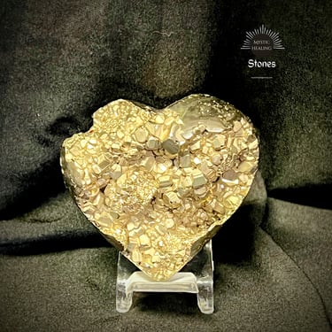 Heart-shaped raw pyrite crystal cluster on a clear display stand against a dark fabric background.