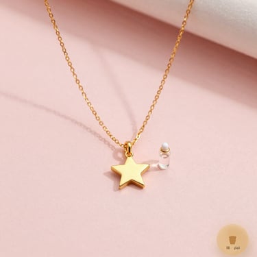 Delicate gold necklace preview on a digital interface, showing options to drag a miniature golden star and a tiny glass vial charm, soft pink background.