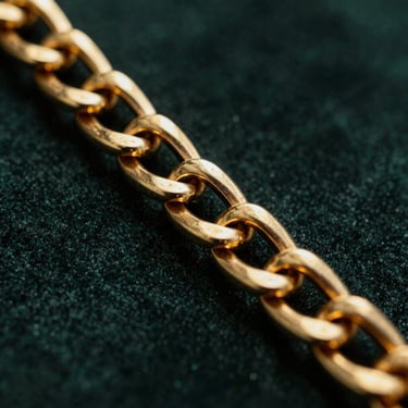Macro details of a heavy 18k gold chain link resting on a dark velvet surface, golden reflections, dark moody lighting