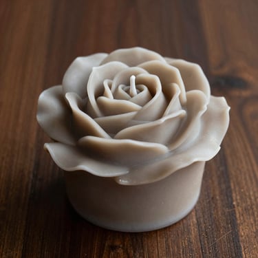 Sculptural wax rose bouquet candle, warm greige tone, styled on dark wood.