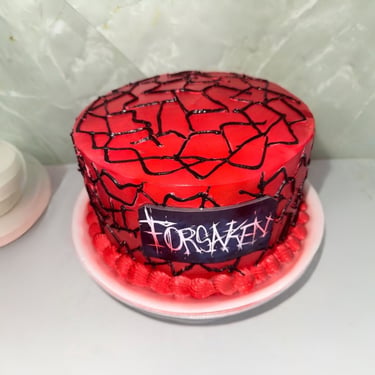 Pastel redondo rojo personalizado con patrones de telaraña negra y una placa con el logotipo de Fors