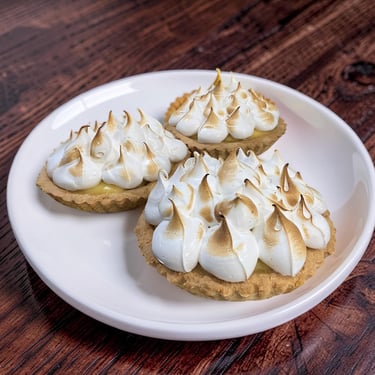 Tres tartas caseras de merengue de limón con picos tostados en un plato blanco sobre un fondo de mad