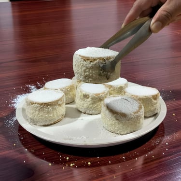 Mano usando pinzas para recoger una galleta redonda de azúcar en polvo de un plato blanco de alfajor