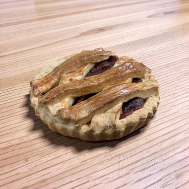 A small lattice-top fruit pie with a golden brown crust on a wooden table.