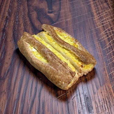 Hojaldre marrón dorado relleno de ensalada de huevo cremosa sobre una mesa de madera oscura.