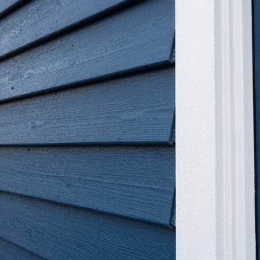 Close-up of crisp paint lines on exterior cedar siding, clean white trim meeting deep blue paint, sharp focus