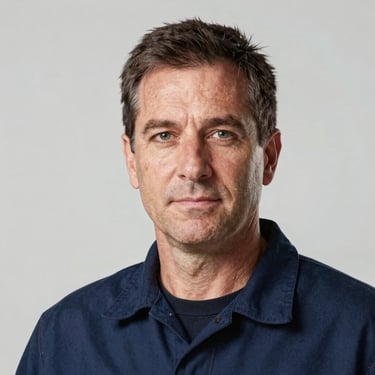 Studio-lit headshot of a middle-aged male electrician in work clothes, direct gaze, neutral light background, authentic professional lighting, no branded t-shirt