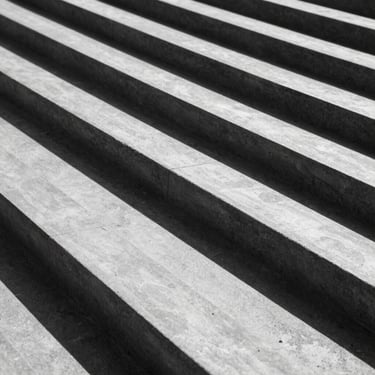 Minimalist macro shot of structured architectural concrete lines casting sharp diagonal shadows under bright sunlight, high-contrast, black and white aesthetic