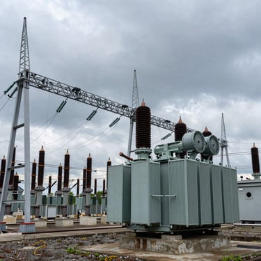 High-contrast wide shot of high-voltage substation transformers and steel gantry structures under a moody, overcast sky, industrial scale.