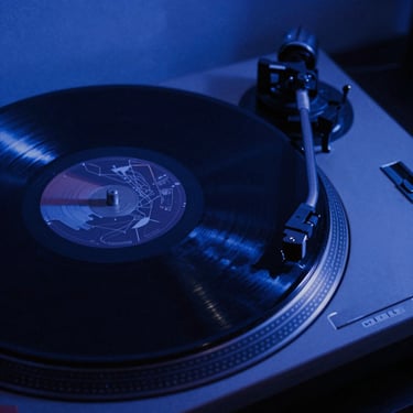 Close-up of a vinyl record spinning on a turntable under low-key blue club lighting, high contrast