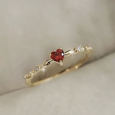 Anillo dorado con piedra en forma de corazón color rojo.