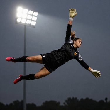 Action freeze-frame of a female goalkeeper diving mid-air against a dark stadium light sky, gritty athletic tone.