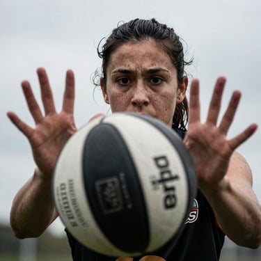 Close-up action shot of a female player shielding the ball, focused intense expression, dramatic overcast daylight.