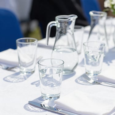 A beautifully set outdoor event table with clean water glasses and pitchers, sunlit.