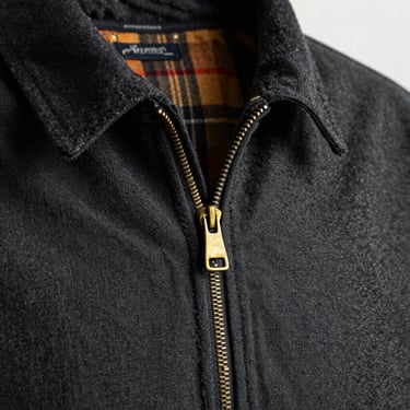 Close-up of a dark charcoal canvas field jacket, brass zipper detail, warm flannel lining visible at the collar