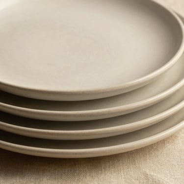 Macro shot of textured handmade ceramic plates stacked on raw linen, soft shadows, warm neutral tones