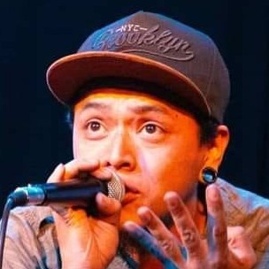 Un artista masculino de hip hop con una gorra snapback de Brooklyn, interpretando en un micrófono.