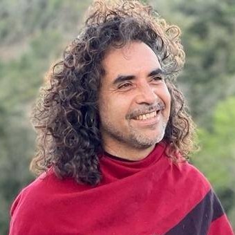 Hombre sonriente con cabello largo, rizado y castaño, usando una camiseta de rayas rojas y negras al