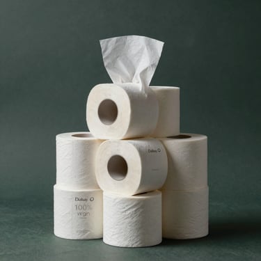 A minimalist studio shot of a stack of Dalisay 100% virgin pulp tissue rolls, glowing under soft light against a dark slate green background, highlighting their purity.