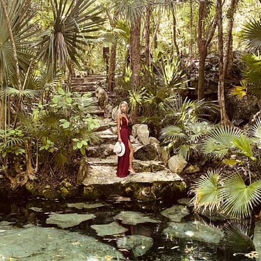 mujer en un cenote usando vestido rojo boho y sombrero en la mano. jungla selva. Tulum