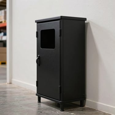 A clean, secure black rodent bait station placed discreetly along a bright warehouse wall, professional setup