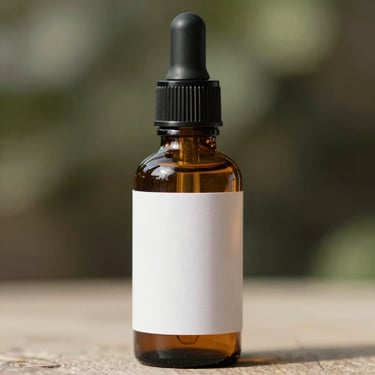 Straight-on close up of amber glass tincture bottle with dropper, minimal white label, natural daylight, soft shadows