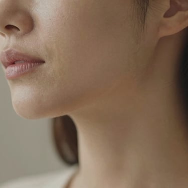Close-up of a woman with radiant, healthy skin, soft natural daylight, elegant muted neutral tones, shallow depth of field