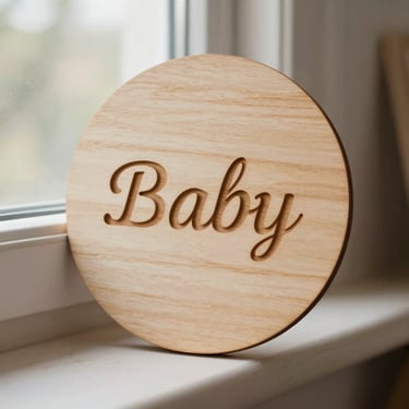 Warm editorial photography of a delicate round wooden birth announcement plaque with engraved baby name, soft natural workshop window light, tactile wood tones, 35mm
