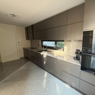 Cuisine contemporaine gris taupe, plan de travail clair, rangements intégrés et électroménager encastré.