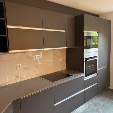 Cuisine moderne gris foncé, crédence effet marbre, électroménager encastré et éclairage intégré.