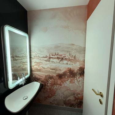 Salle d’eau avec lavabo mural, miroir lumineux et fresque décorative aux tons chauds.