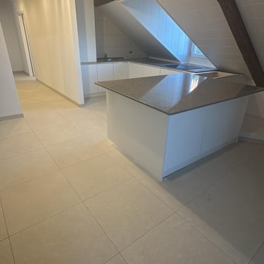 Cuisine sous combles blanche avec îlot central et plan de travail en pierre naturelle.