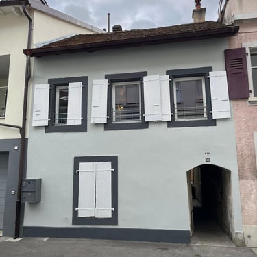 Façade de maison rénovée avec volets blancs, encadrements gris et passage voûté.