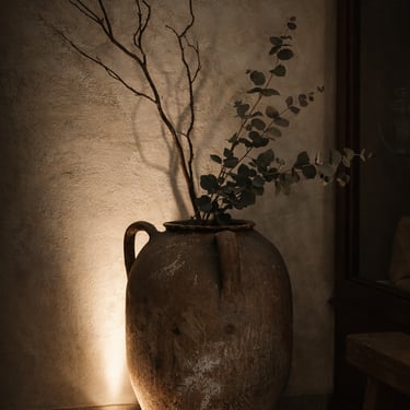 Decorazione d'interni stile wabi-sabi: giara in terracotta con rami decorativi e luce d'accento su muro texturizzato