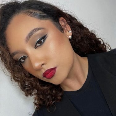 Mujer con cabello castaño rizado que luce un atrevido lápiz labial rojo y un llamativo delineador