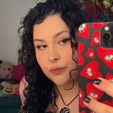 Mujer joven con cabello negro rizado y piercings faciales tomándose una selfie