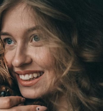 Smiling blonde woman with wavy hair and heart-patterned manicure holding her beautiful pet dog.