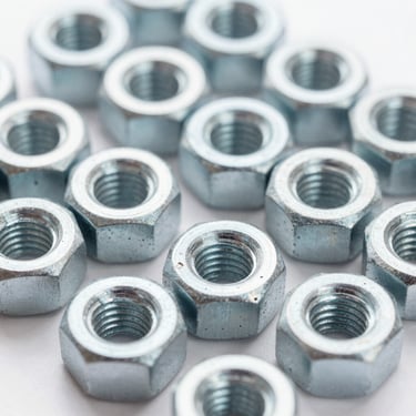 Close-up of industrial steel hex nuts and threaded bushings, bright clean factory lighting, metallic steel tones, macro lens