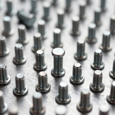 Macro shot of solid steel rivets, pins, and custom shafts on a clean metal surface, sharp industrial product photography