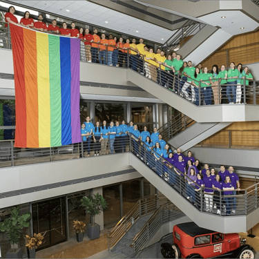 EQUAL ERG Summit attendees in rainbow-colored shirts posing together on a stairway.
