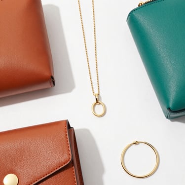 Top-down flat lay of minimalist fashion accessories, leather goods, and modern jewelry, bright high-key retail photography, clean natural daylight