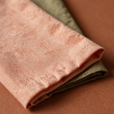 Softly folded premium linen napkins in peach and olive tones, textured fabric detail