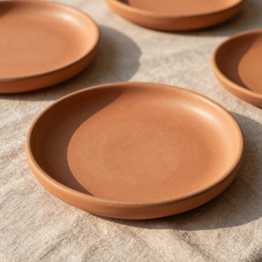 Close-up of textured ceramic charger plates in warm terracotta tones on a neutral linen tablecloth