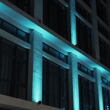 Night shot of a modern building facade with architectural accent lighting in cyan and dark blue tones.