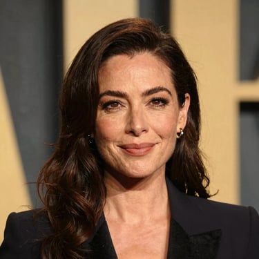 A professional portrait of a woman with a warm, engaged expression, photographed in soft theater lighting in the Pacific Northwest US. Elegant attire and a sophisticated backdrop.